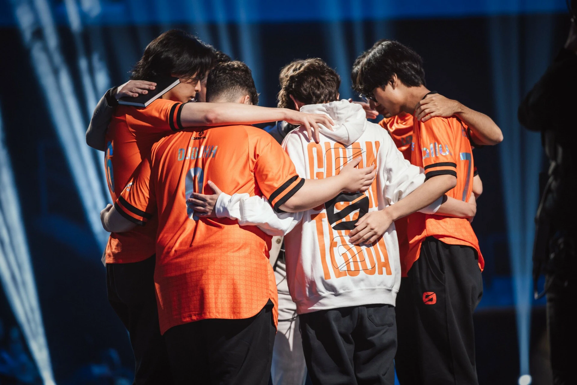 LOS players huddling together on stage in orange jerseys and a white LOS jacket